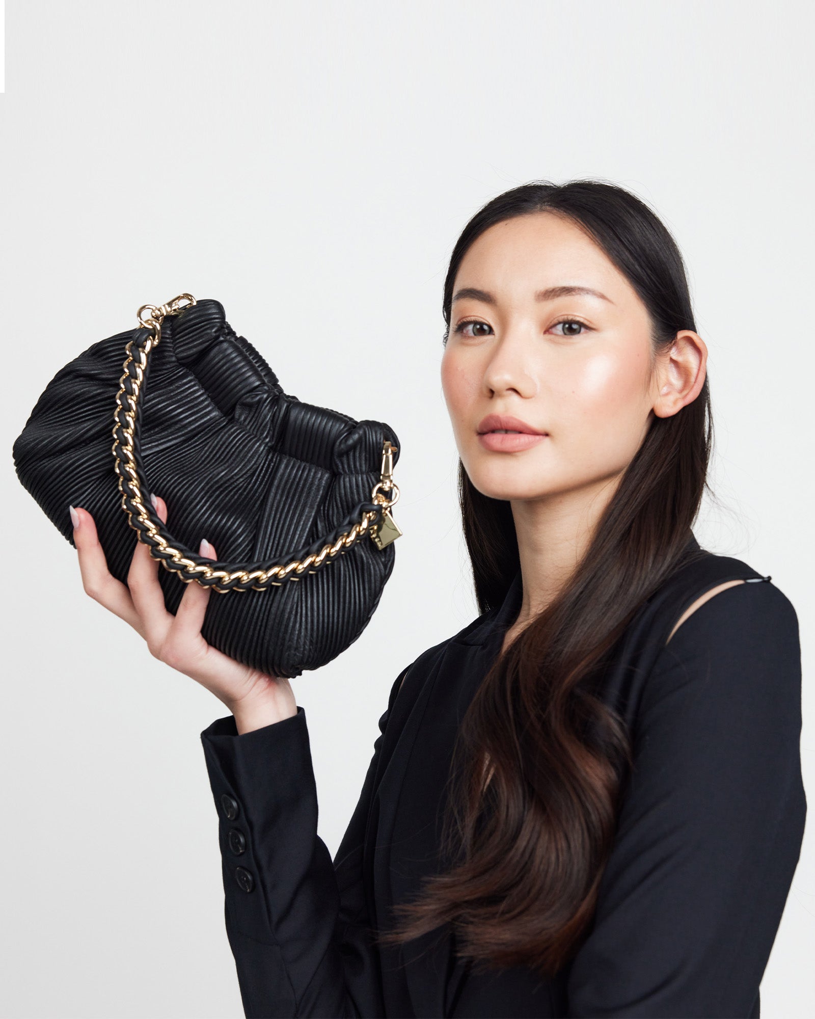 A person wearing a white outfit holding a beige bag with a gold chain feature handle draped across the front.